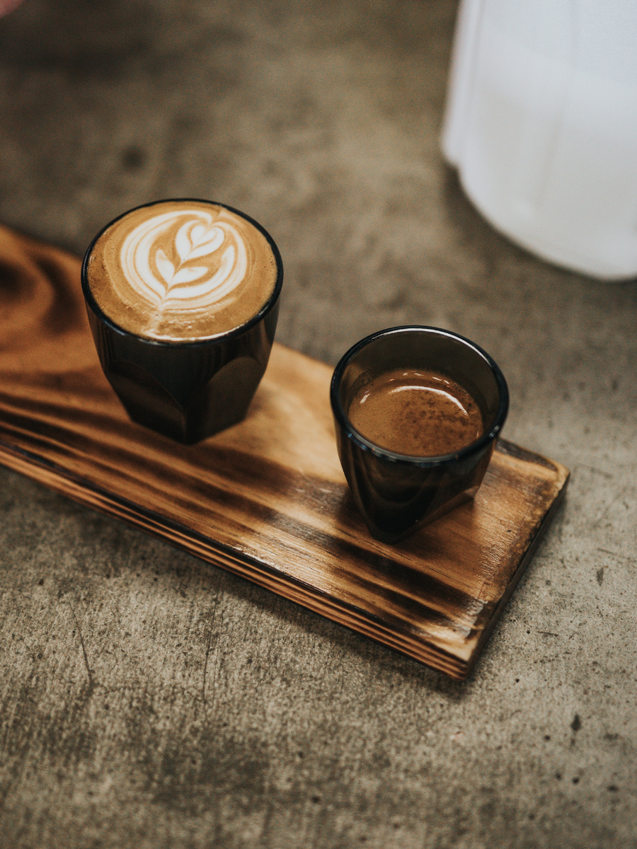 Cappuccino met latte art en een espresso op een houten plankje